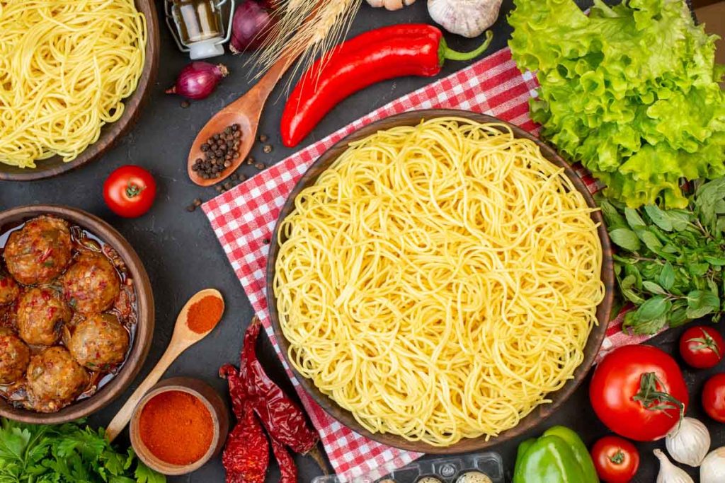 top view tasty spaghetti in bowls meatball soup in bowl lettuce wooden spoons tomato on table